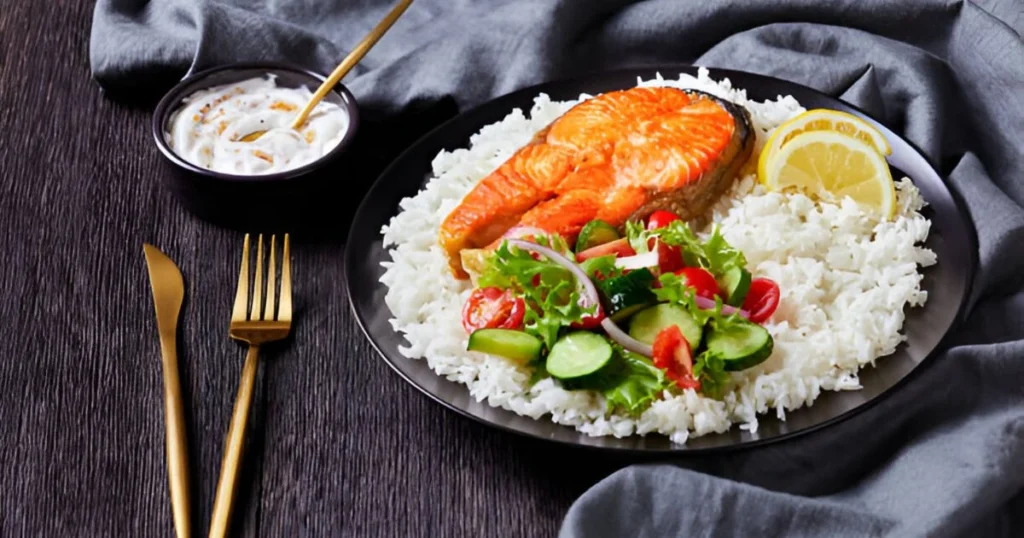 A plate of perfectly cooked salmon fillet served over fluffy rice with a garnish of fresh herbs and lemon slices.