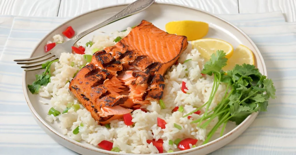 A plate of perfectly cooked salmon fillet served over fluffy rice with a garnish of fresh herbs and lemon slices.